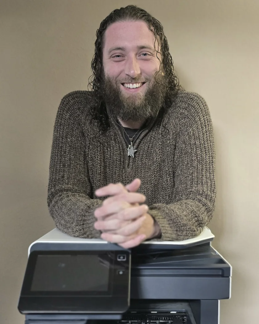 Ochre Entwhistle, smiling, arms folded on top of an office printer